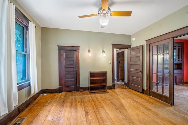 unfurnished room with wood-type flooring, visible vents, ceiling fan, and baseboards