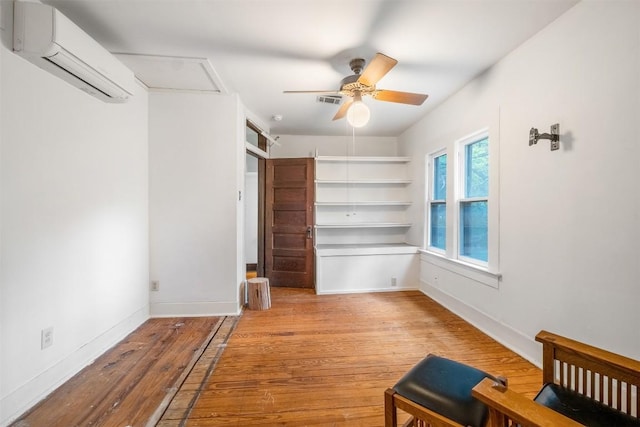 interior space featuring a ceiling fan, visible vents, baseboards, an AC wall unit, and wood-type flooring