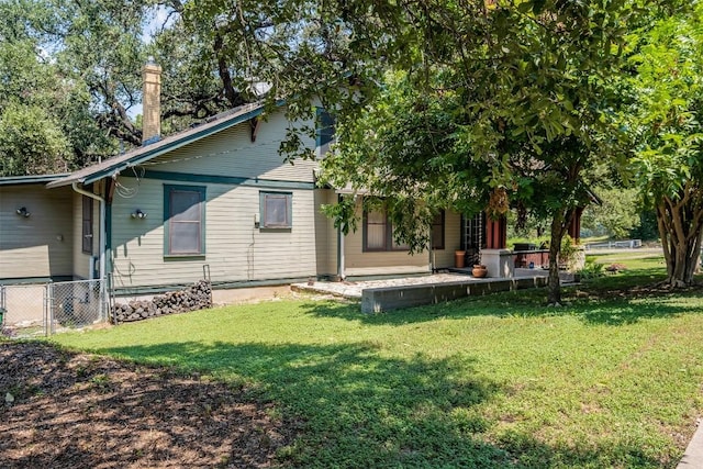 rear view of property with a lawn, a chimney, and fence