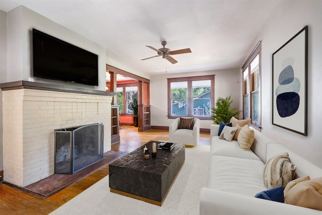 living room featuring a brick fireplace, hardwood / wood-style floors, and ceiling fan