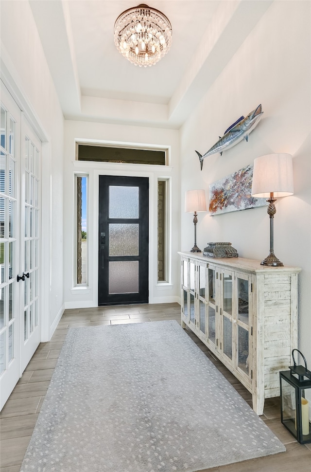 foyer with a raised ceiling, french doors, plenty of natural light, and a chandelier