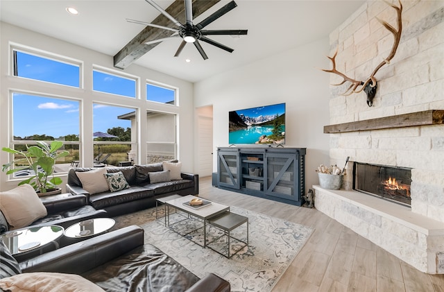 living room with ceiling fan, beam ceiling, and a stone fireplace