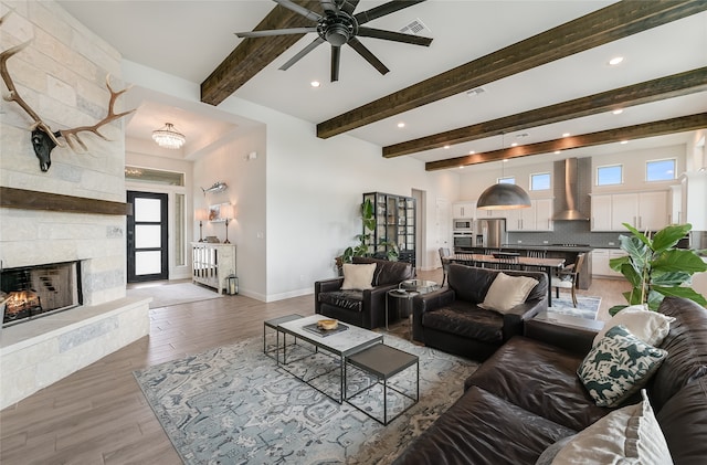 living room with ceiling fan, a fireplace, wood-type flooring, and beamed ceiling