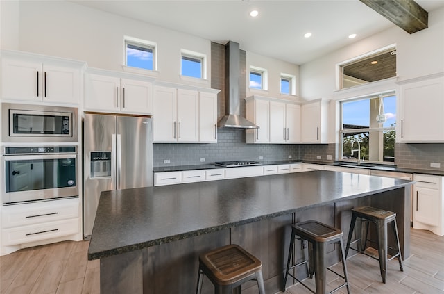 kitchen featuring appliances with stainless steel finishes, white cabinetry, and wall chimney range hood