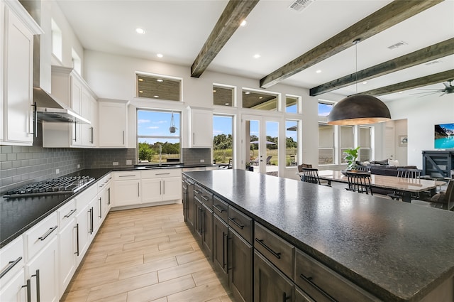 kitchen with decorative light fixtures, backsplash, a kitchen island, white cabinetry, and stainless steel gas cooktop