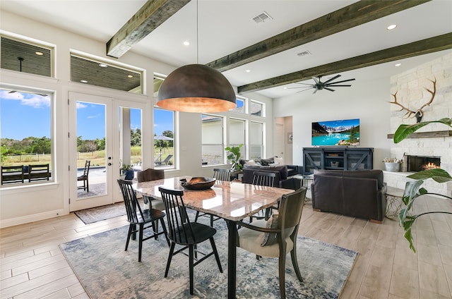 dining space with ceiling fan, beamed ceiling, french doors, and a fireplace