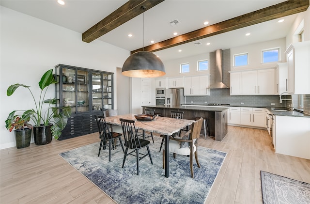 dining space with beamed ceiling, light hardwood / wood-style flooring, and sink