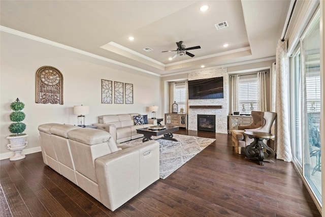 living area with a stone fireplace, a tray ceiling, dark wood finished floors, and visible vents