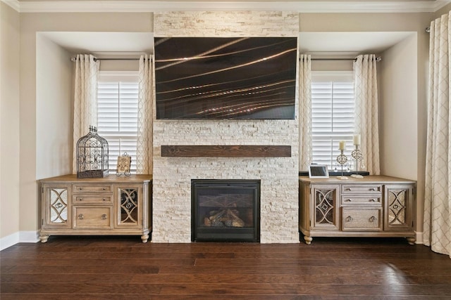 living room featuring baseboards, ornamental molding, dark wood-type flooring, and a stone fireplace