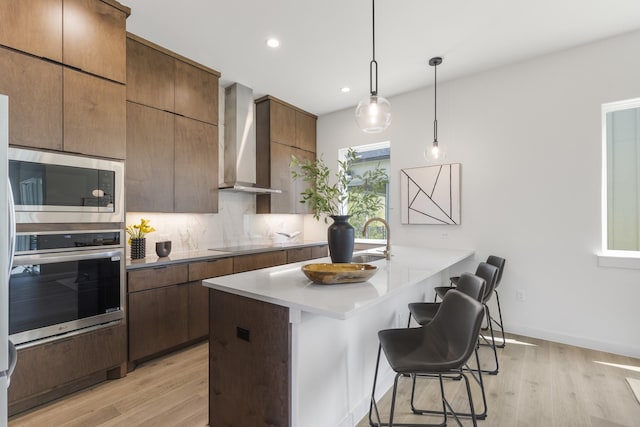 kitchen featuring decorative backsplash, oven, a kitchen breakfast bar, built in microwave, and wall chimney range hood