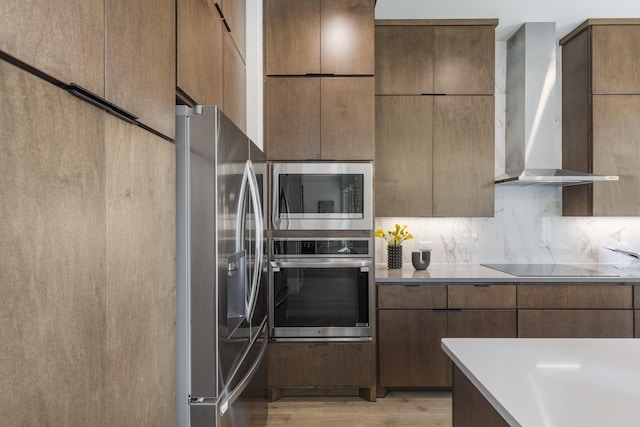 kitchen featuring appliances with stainless steel finishes, wall chimney exhaust hood, light hardwood / wood-style flooring, and backsplash