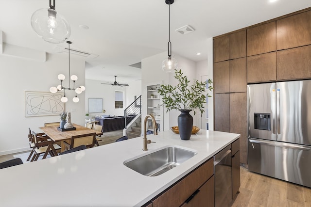 kitchen with ceiling fan, sink, light wood-type flooring, appliances with stainless steel finishes, and an island with sink