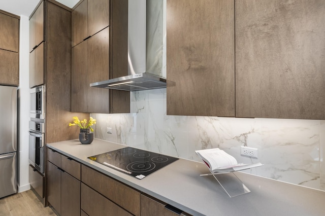 kitchen featuring decorative backsplash, wall chimney exhaust hood, stainless steel appliances, and light hardwood / wood-style flooring