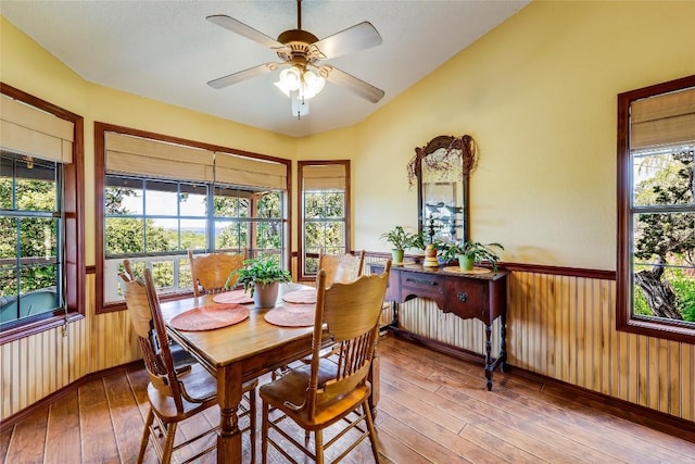 dining space with a wainscoted wall, radiator, wood-type flooring, a ceiling fan, and wooden walls