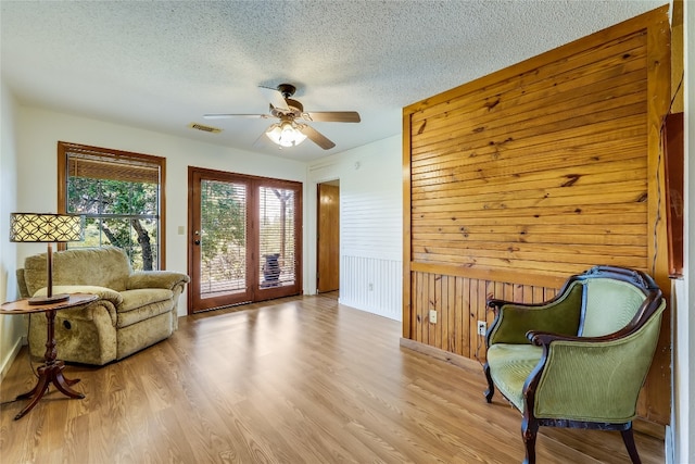 sitting room with a textured ceiling, wood walls, wood finished floors, visible vents, and a ceiling fan