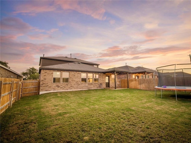 245 Tulum Ter, Leander, TX 78641 - back of property at dusk with a trampoline, brick siding, and a fenced backyard
