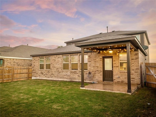 245 Tulum Ter, Leander, TX 78641 - back of property at dusk featuring a patio, a fenced backyard, brick siding, and a shingled roof