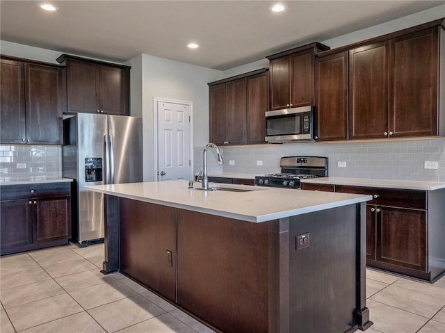245 Tulum Ter, Leander, TX 78641 - kitchen featuring appliances with stainless steel finishes, light tile patterned floors, decorative backsplash, dark brown cabinets, and an island with sink