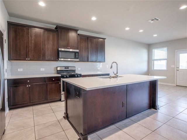245 Tulum Ter, Leander, TX 78641 - kitchen with appliances with stainless steel finishes, backsplash, light countertops, a center island with sink, and dark brown cabinets