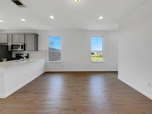 interior space featuring gray cabinetry, decorative backsplash, stove, and hardwood / wood-style flooring