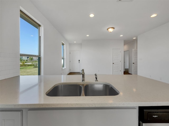 kitchen with light stone countertops, sink, and dishwashing machine