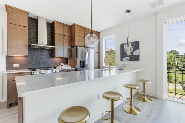 kitchen with appliances with stainless steel finishes, a healthy amount of sunlight, decorative light fixtures, and wall chimney range hood