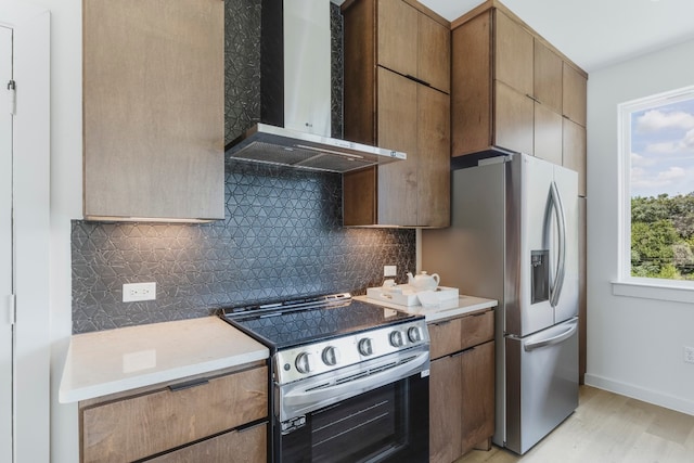 kitchen with appliances with stainless steel finishes, light hardwood / wood-style flooring, backsplash, and wall chimney range hood