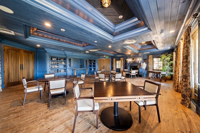 dining room with built in shelves, a tray ceiling, crown molding, and light hardwood / wood-style flooring