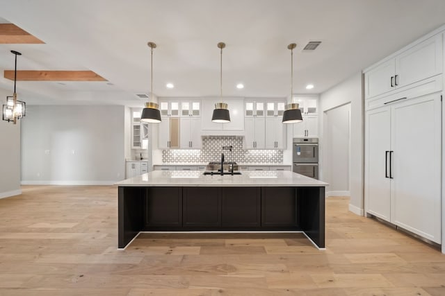 kitchen featuring white cabinets, double oven, a large island with sink, and light hardwood / wood-style floors