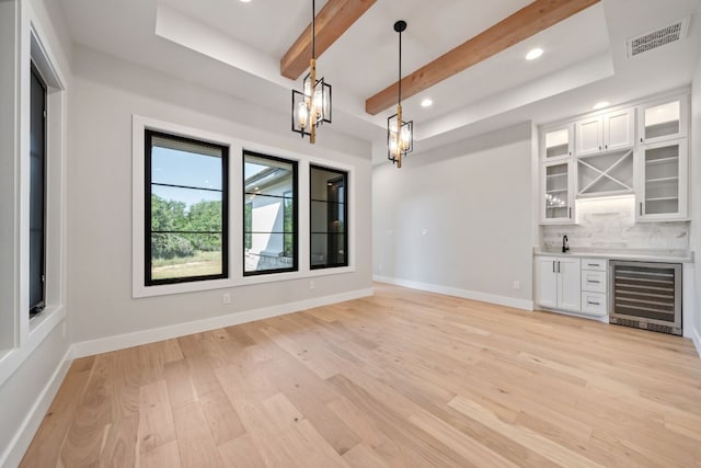 unfurnished dining area featuring an inviting chandelier, beverage cooler, beam ceiling, sink, and light wood-type flooring