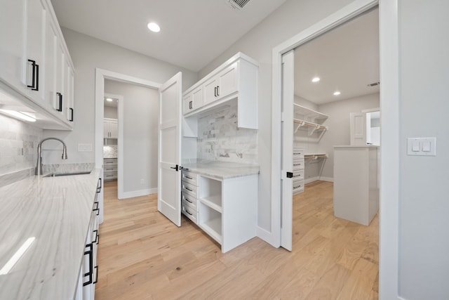 kitchen with white cabinets, backsplash, light wood-type flooring, light stone counters, and sink