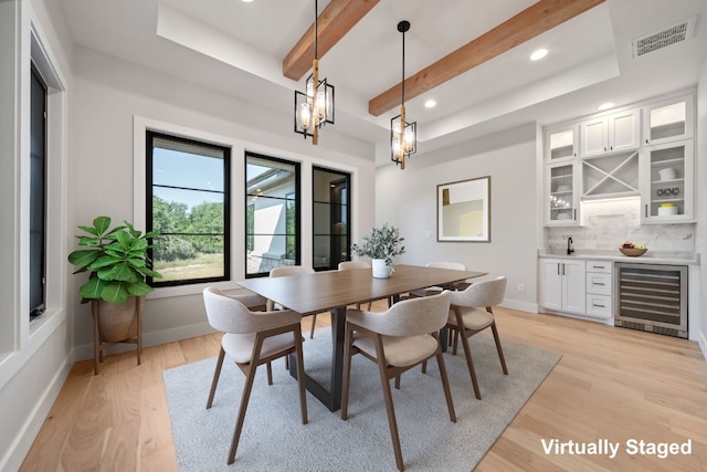 dining area with light wood-type flooring, an inviting chandelier, wine cooler, and beamed ceiling