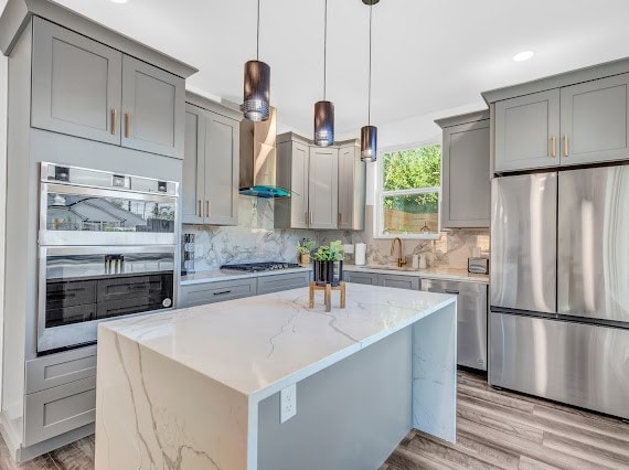 kitchen featuring appliances with stainless steel finishes, light hardwood / wood-style flooring, light stone counters, backsplash, and a kitchen island