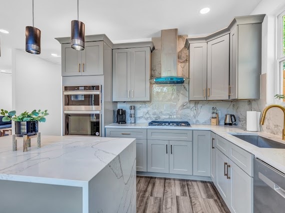 kitchen with hardwood / wood-style floors, appliances with stainless steel finishes, wall chimney exhaust hood, decorative backsplash, and sink