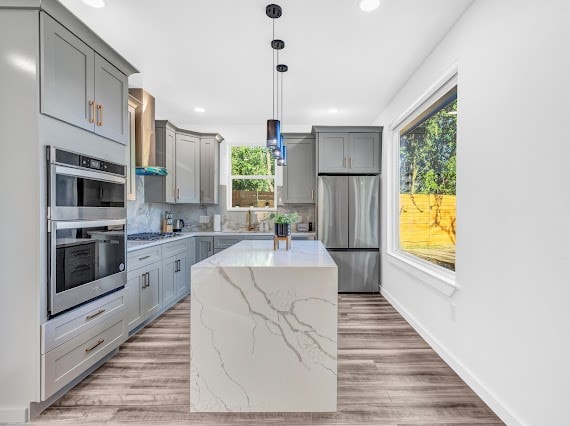 kitchen with a center island, light stone counters, hanging light fixtures, hardwood / wood-style floors, and appliances with stainless steel finishes