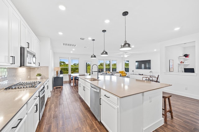 kitchen with stainless steel appliances, sink, dark hardwood / wood-style floors, ceiling fan, and a center island with sink