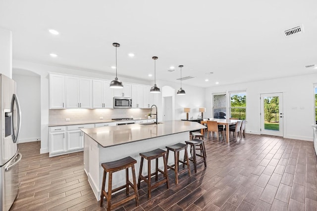 kitchen featuring white cabinets, appliances with stainless steel finishes, a kitchen island with sink, light countertops, and pendant lighting