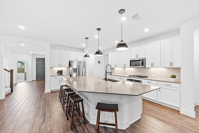 kitchen featuring white cabinets, stainless steel appliances, a center island with sink, and sink