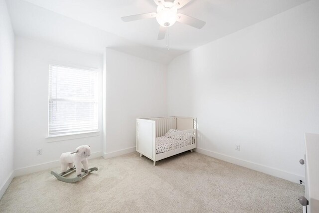 unfurnished bedroom with light colored carpet, vaulted ceiling, a crib, and ceiling fan