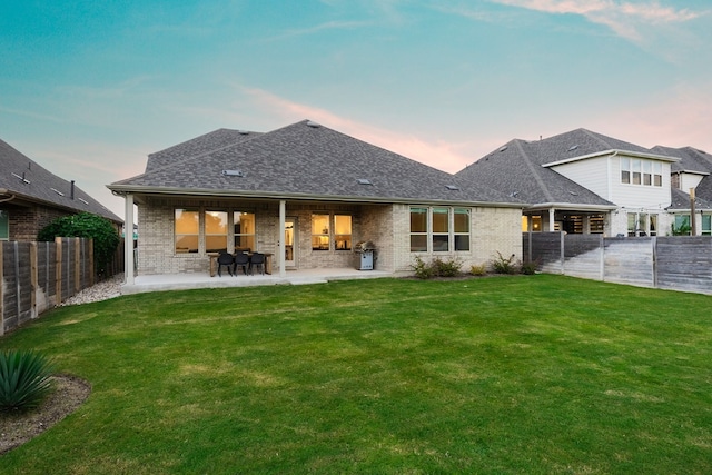 back house at dusk with a lawn and a patio area