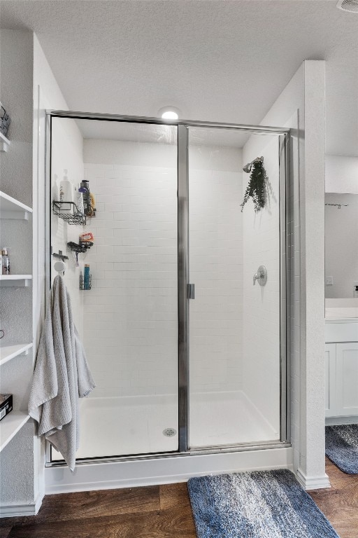 bathroom with a textured ceiling, a shower with door, and wood-type flooring