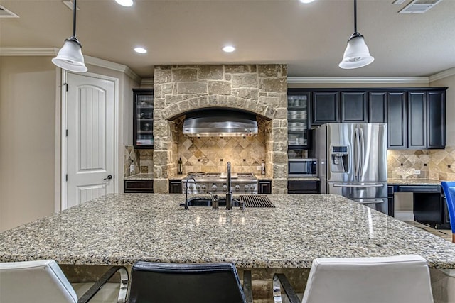 kitchen featuring a kitchen island with sink, stainless steel appliances, a sink, ornamental molding, and tasteful backsplash