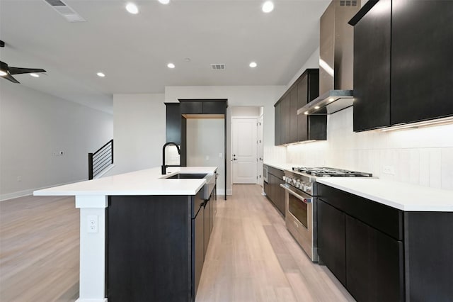 kitchen featuring sink, high end stainless steel range oven, light hardwood / wood-style flooring, ceiling fan, and an island with sink