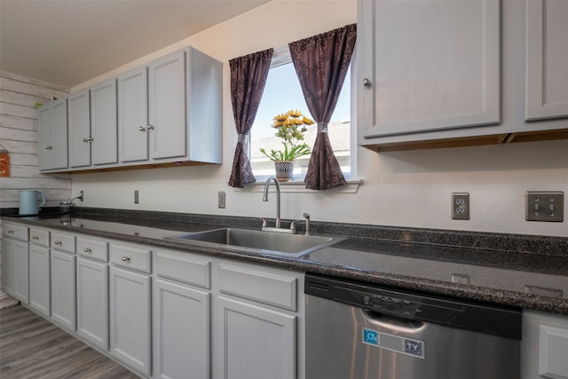 kitchen with dark stone counters, dishwasher, light wood-type flooring, and sink