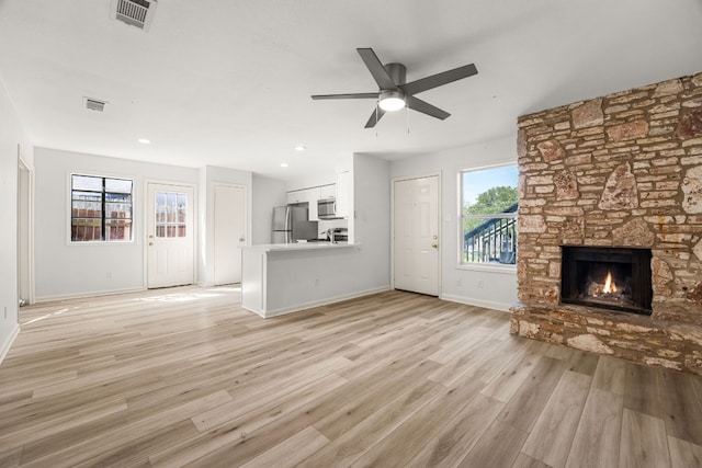 unfurnished living room featuring ceiling fan, light hardwood / wood-style flooring, and a stone fireplace