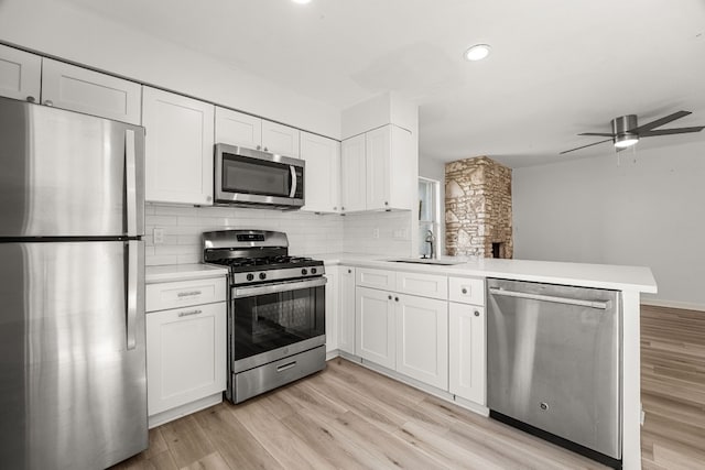 kitchen with stainless steel appliances, tasteful backsplash, kitchen peninsula, white cabinetry, and light hardwood / wood-style flooring