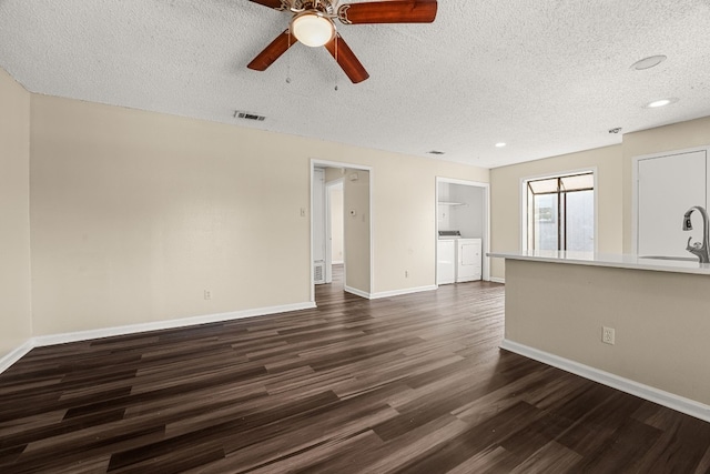 unfurnished living room featuring ceiling fan, washer and dryer, sink, dark hardwood / wood-style floors, and a textured ceiling