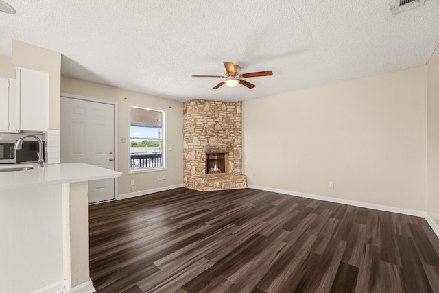 unfurnished living room with ceiling fan, a stone fireplace, sink, dark hardwood / wood-style flooring, and a textured ceiling