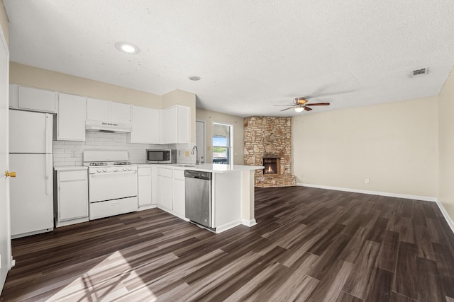 kitchen with kitchen peninsula, a stone fireplace, a textured ceiling, dark wood-type flooring, and stainless steel appliances