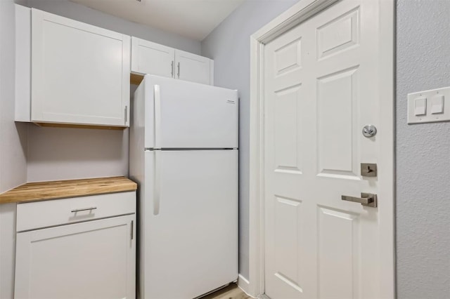 kitchen featuring white cabinets, white refrigerator, and butcher block counters